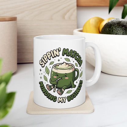 White ceramic matcha mug with a kawaii matcha-cup character and the text “Sippin’ Matcha Minding My Business
