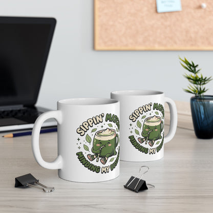White ceramic matcha mug with a kawaii matcha-cup character and the text “Sippin’ Matcha Minding My Business, view of both sides of the mug