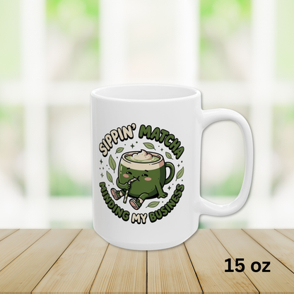 Close-up view of 15oz White ceramic matcha mug with a kawaii matcha-cup character and the text “Sippin’ Matcha Minding My Business