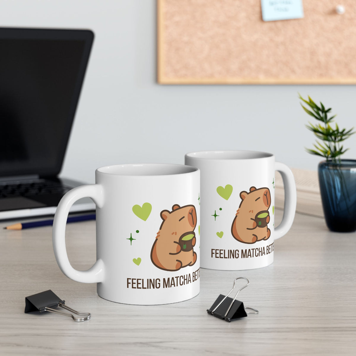 White ceramic matcha mug with a cute capybara drinking green tea, surrounded by hearts and stars, and the text “Feeling Matcha Better,” view of both sides