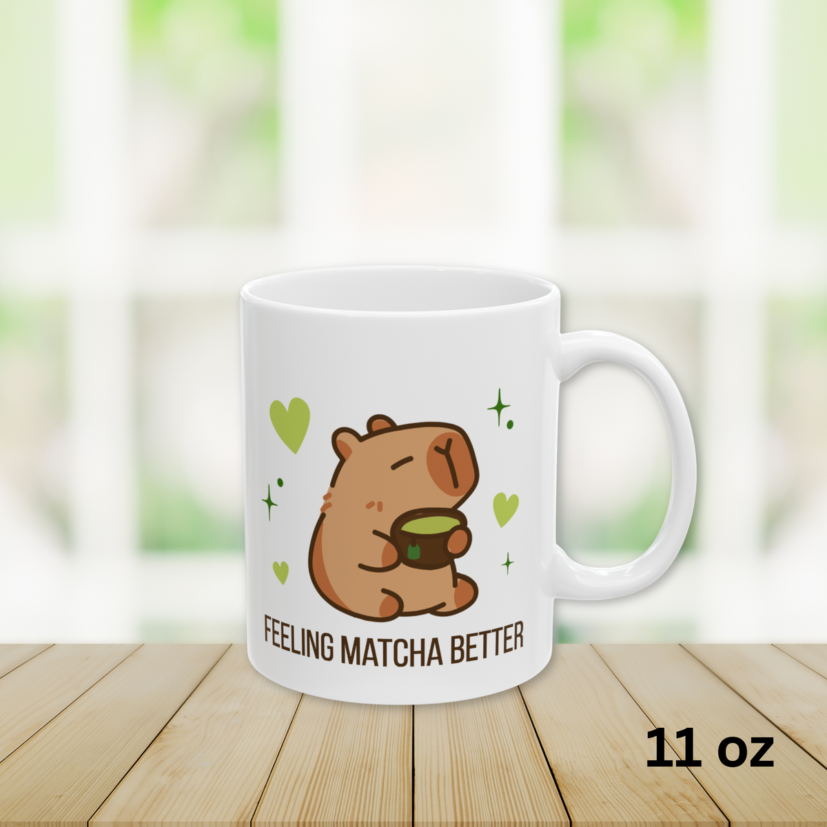 Close-up of a white ceramic matcha mug with a cute capybara drinking green tea, surrounded by hearts and stars, and the text “Feeling Matcha Better,” 11oz