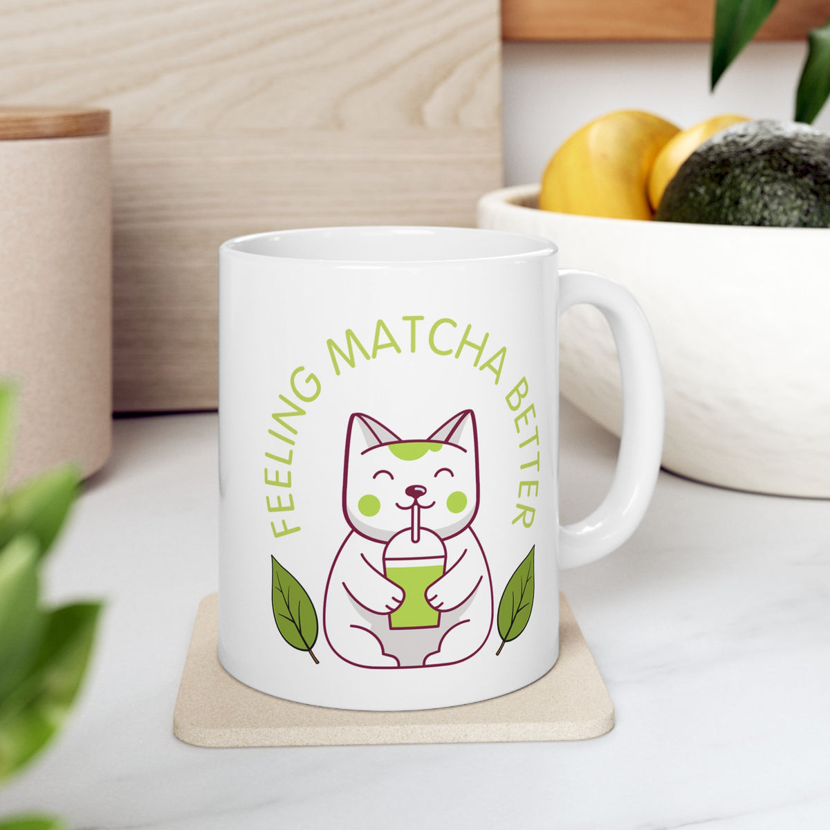 White ceramic matcha mug with a cute cat drinking matcha and the text “Feeling Matcha Better,” resting on a coaster on a kitchen counter