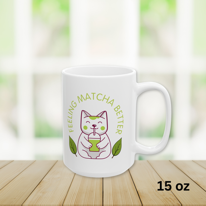 Close-up of a white ceramic matcha mug with a cute cat drinking matcha and the text “Feeling Matcha Better, ” 15 oz