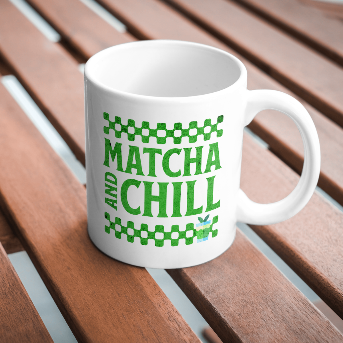 White ceramic matcha mug with a checkered border above and below the text “Matcha and Chill," resting on a wooden table