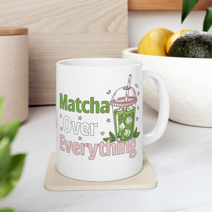 White ceramic matcha mug with an iced matcha latte illustration surrounded by tiny hearts and stars and the text “Matcha Over Everything,” resting on a trivet on a kitchen counter