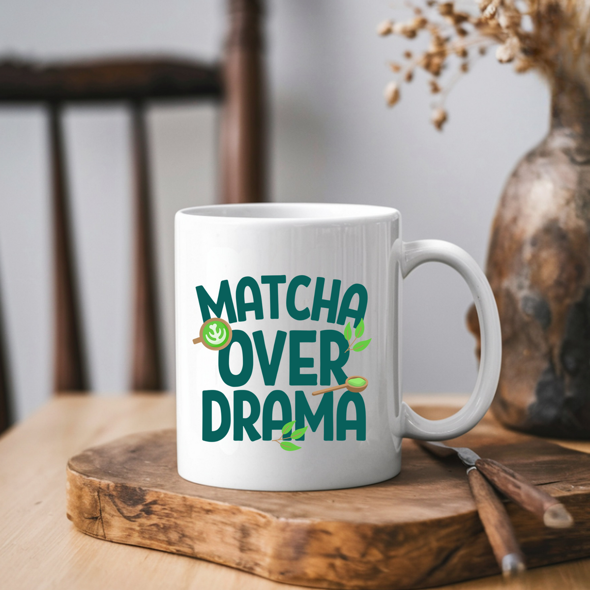 White ceramic "Matcha Over Drama" coffee mug with mini images of green tea leaves, a matcha latte, and wooden spoon filled with matcha powder,  sitting on a wooden cutting board