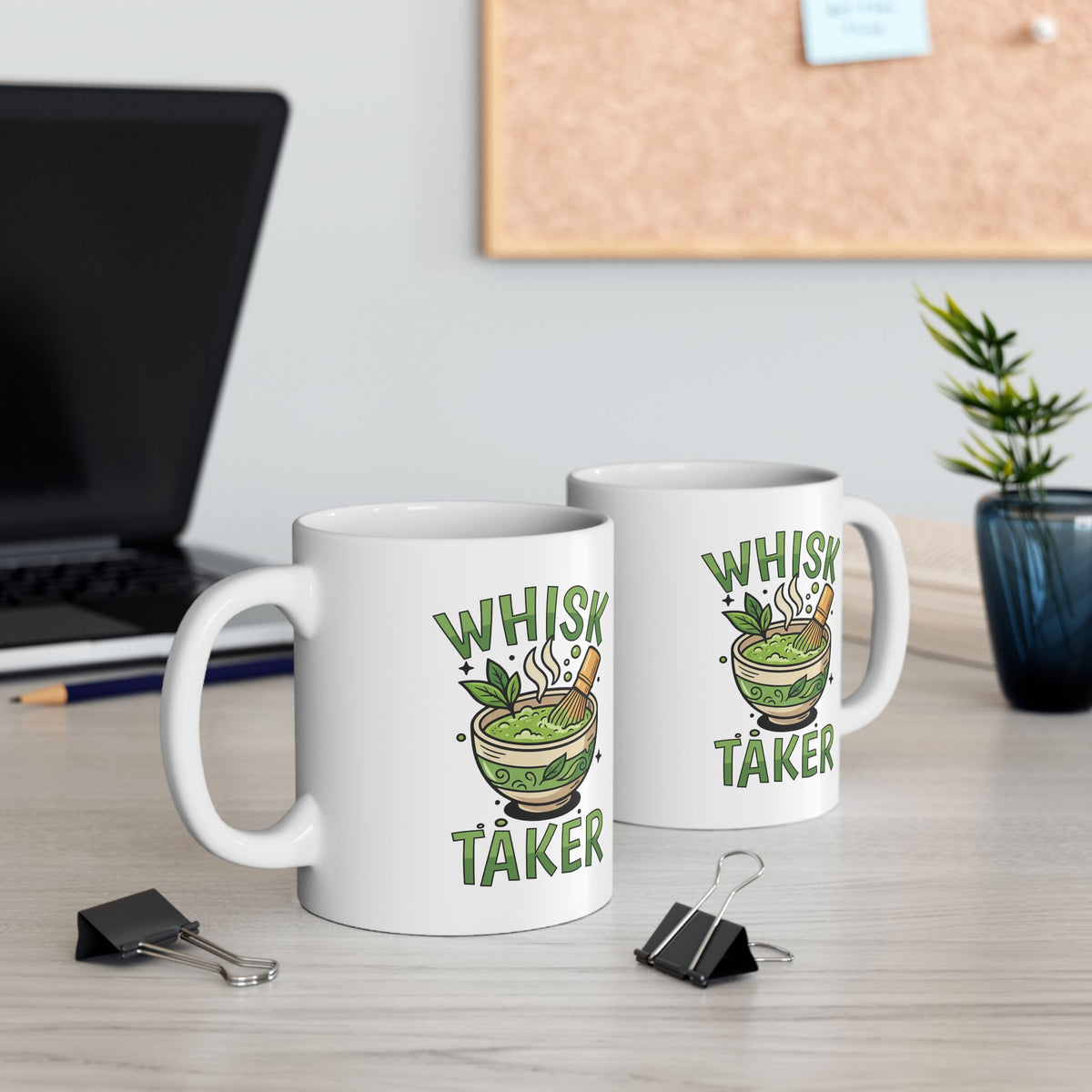 White ceramic mug with the text “Whisk Taker” and an illustration of a steaming matcha bowl with a bamboo whisk and tea leaves, view of both sides of the mug
